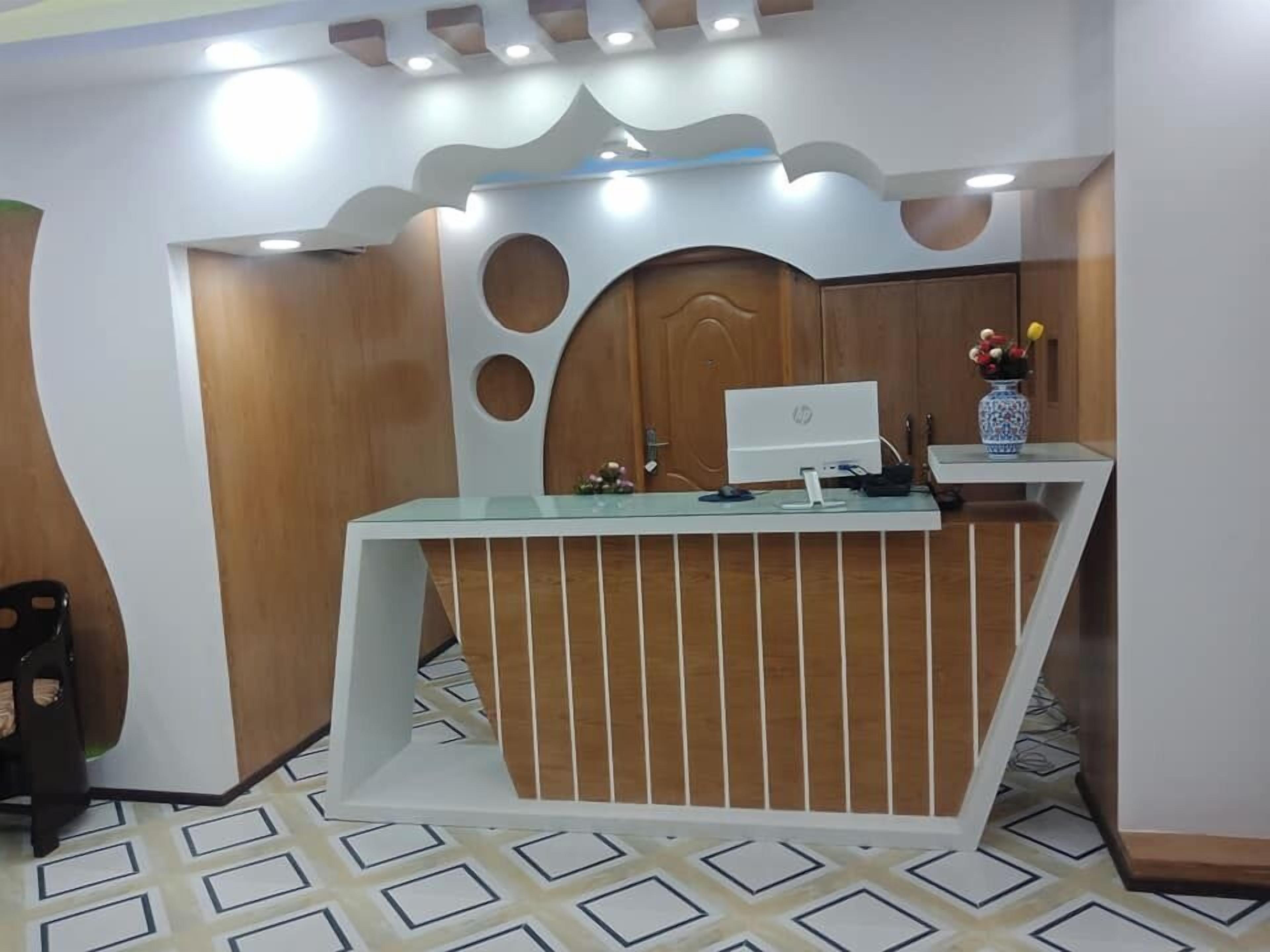 A reception desk with a computer, a vase with flowers, and a patterned floor.
