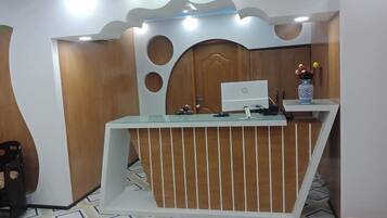 A reception desk with a computer, a vase with flowers, and a patterned floor.