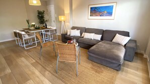 Una sala de estar moderna con un sofá seccional gris, sillas de mimbre, una mesa de comedor con sillas, un tapiz tejido y un cuadro en la pared.