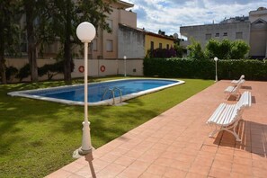 Piscina con borde de baldosas, rodeada de césped y árboles.