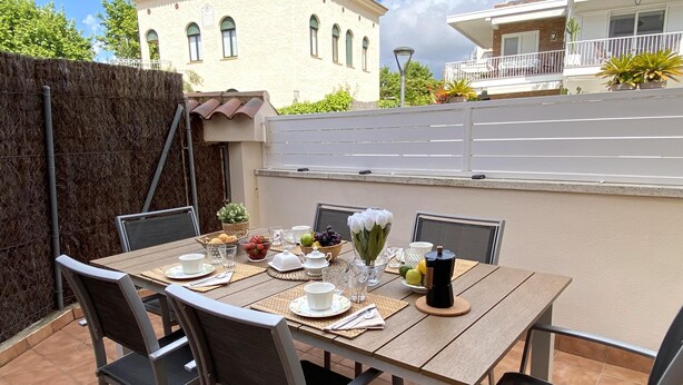 Un área de comedor al aire libre con una mesa de madera dispuesta para cuatro personas, rodeada de sillas.