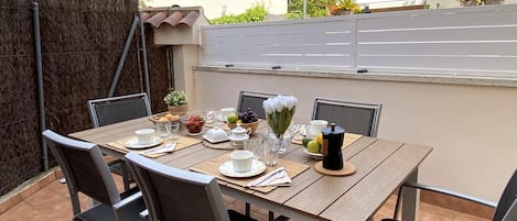 Ein Essbereich im Freien mit einem Holztisch, gedeckt für vier Personen, umgeben von Stühlen.