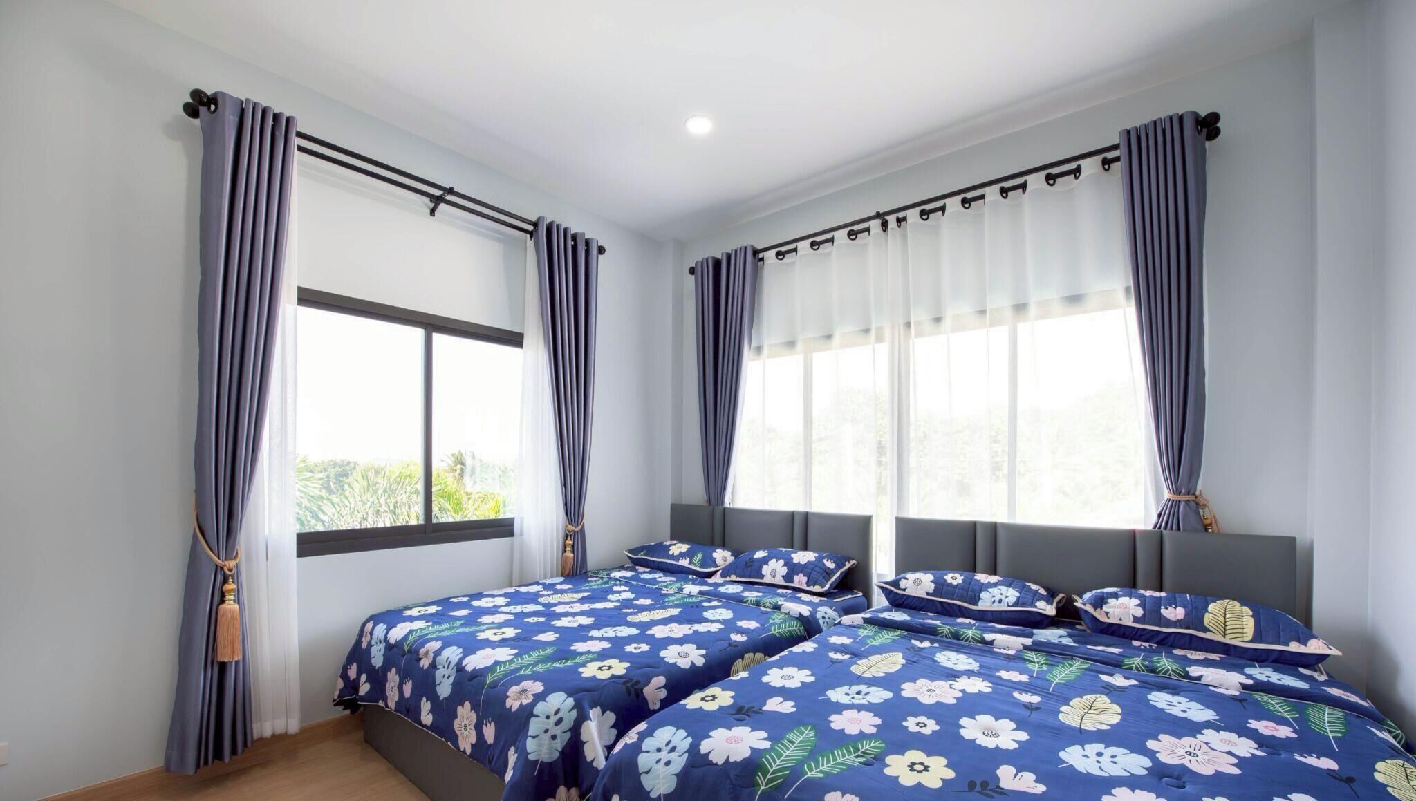 Une chambre avec deux lits, de grandes fenêtres avec des rideaux et une vue sur la verdure environnante.