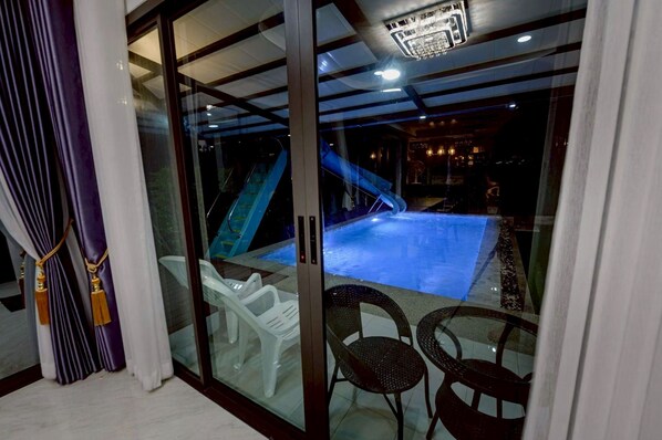 A glass-enclosed room with a pool, a slide, and two wicker chairs.