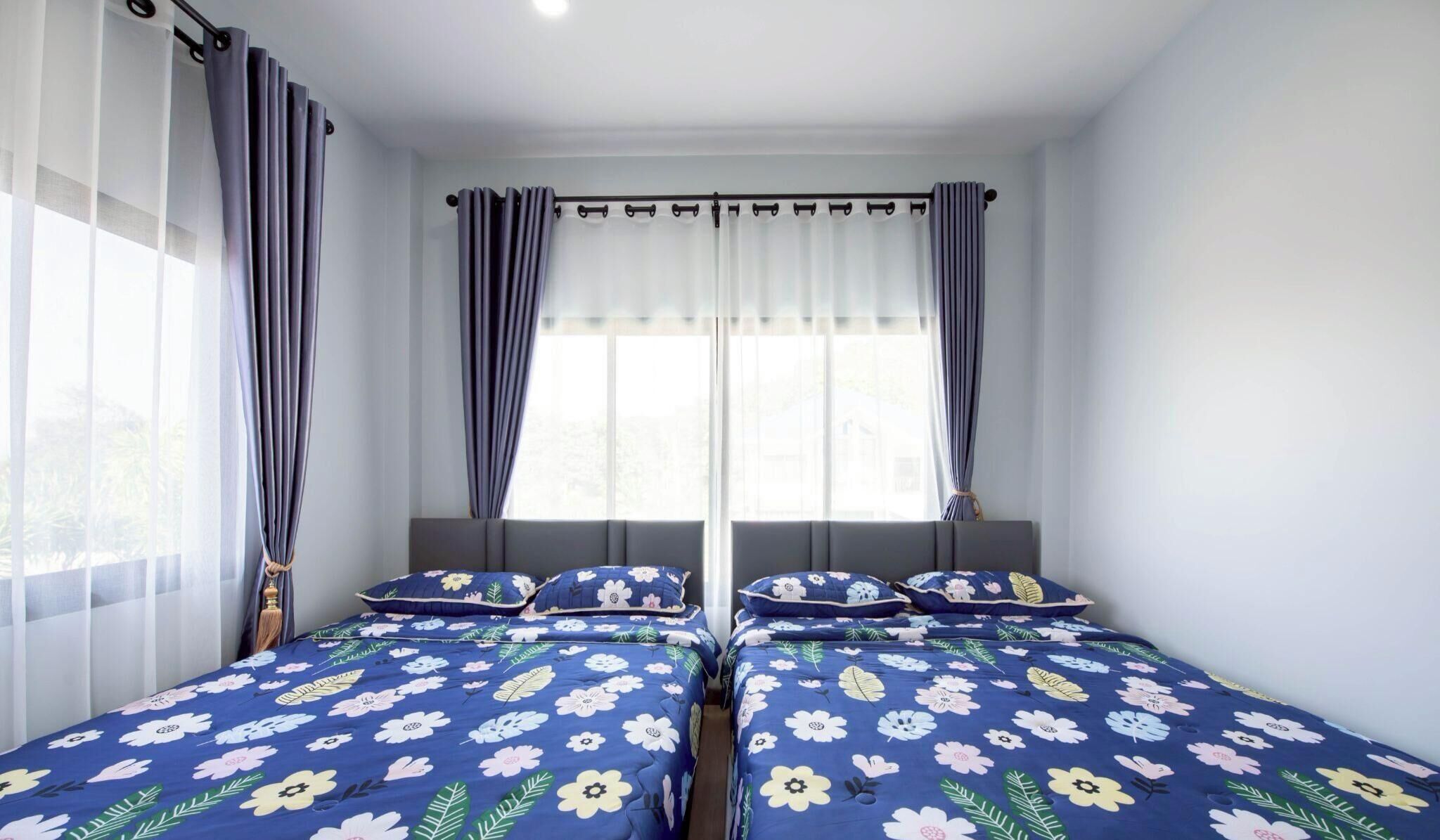 A room with two beds, sheer curtains, and a window with a view.