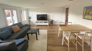 Een woonkamer met een bank, salontafel, televisie en een eethoek met stoelen en een tafel.