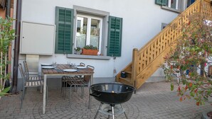 Een terras met een tafel, stoelen, een barbecue en een trap.
