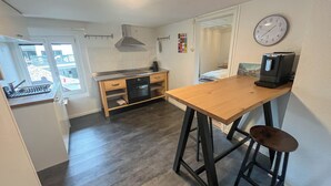 Een kleine keuken met een houten tafel, een koffiezetapparaat en een klok aan de muur.