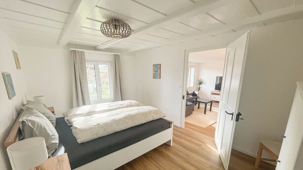 Een moderne slaapkamer met een bed, nachtkastje, lamp en uitzicht op een zithoek.