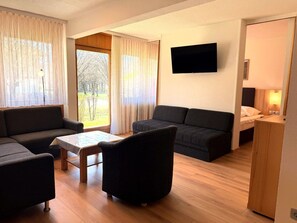 Ein modernes Wohnzimmer mit einer Couch, Sesseln, einem Couchtisch und einem an der Wand befestigten Flachbildfernseher.