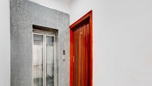 A hallway with a glass elevator door and a wooden door with a number plate. - Collection O Sector 1 Manesar (Gurugram)