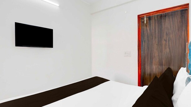 A modern hotel room with a bed, a flat-screen TV mounted on the wall, and a wooden door. - Collection O Sector 1 Manesar (Gurugram)