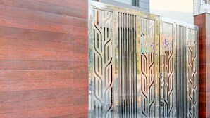 A metal gate with intricate cut-out patterns, a wooden wall, and a tiled floor. - Collection O Sector 1 Manesar (Gurugram)