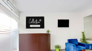 A reception area with a brown reception desk, a blue sofa, and a potted plant. - Collection O Sector 1 Manesar (Gurugram)