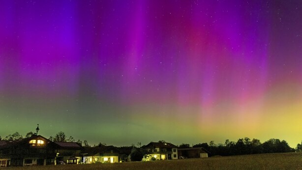 Landskab med huse under en nattehimmel med nordlys.