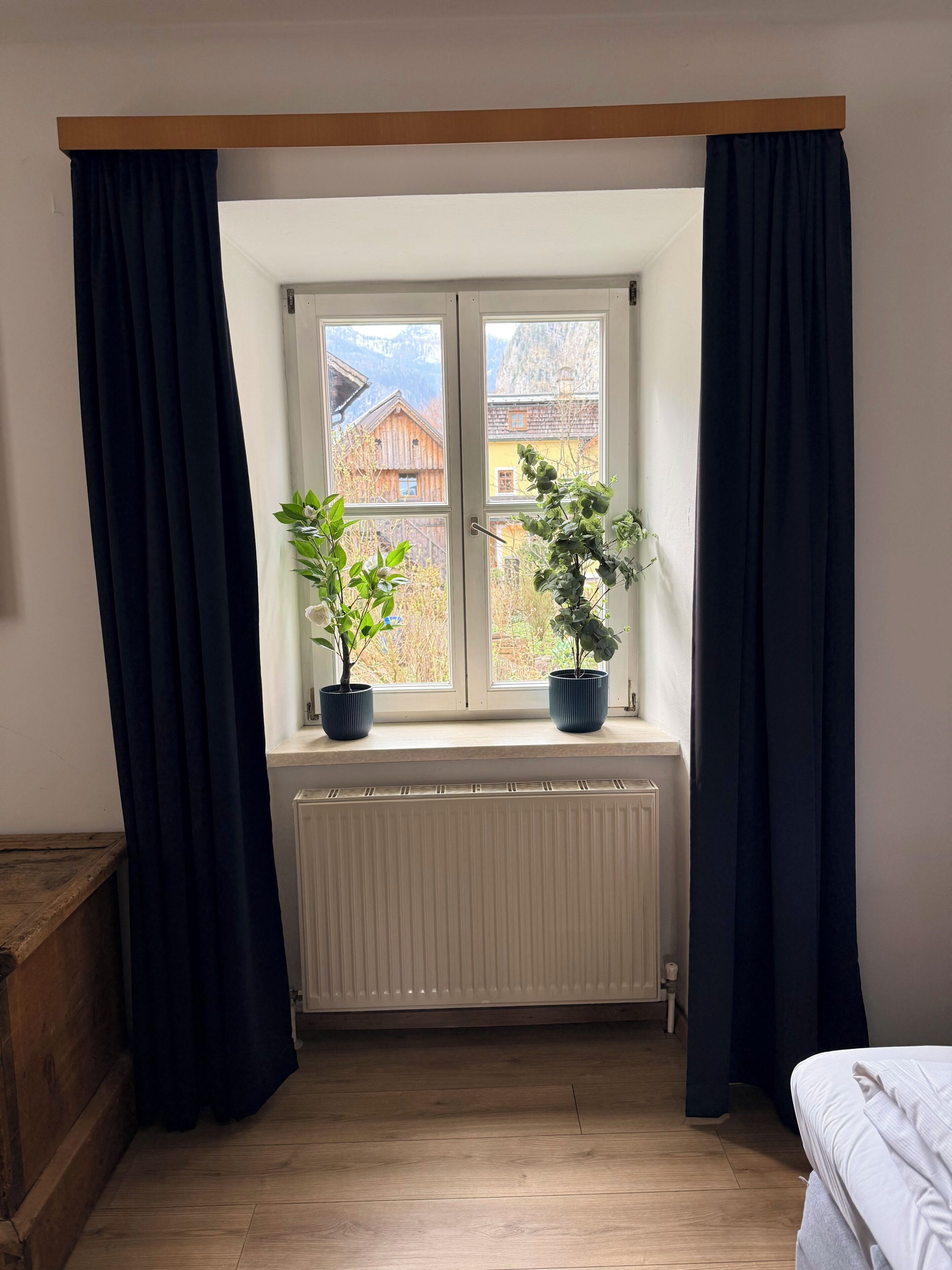 Ein Zimmer mit Fenster, zwei Blumentöpfen, einem Heizkörper und Holzboden.