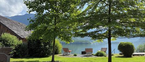 A lakeside property with a wooden cabin, a grassy lawn, and two wooden chairs by the water.