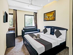 A hotel room with a bed, a sofa, a TV, a window with curtains, and a painting on the wall. - Townhouse Prakash Continental (New Delhi)