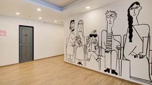 A spacious room with a high ceiling, a wooden floor, and a wall mural depicting abstract figures. A door with room numbers is visible. - Townhouse Prakash Continental (New Delhi)