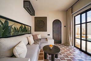 Una sala moderna con un sofá, una mesa redonda con un frutero, un ventanal con vista a una piscina y una puerta con diseño circular.