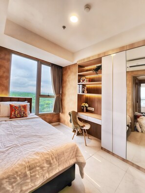 A bedroom with a large bed, a desk, and a wardrobe. - Golden By SanLiving - 2BR - PIK (Jakarta)