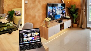 Un salon moderne doté d’un téléviseur à écran plat, d’un ordinateur portable et d’un coin repas avec une table et des chaises.