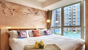 Une chambre d’hôtel moderne, dotée d’un grand lit, d’une fresque murale décorative et offrant une vue sur le paysage urbain grâce à de grandes fenêtres.