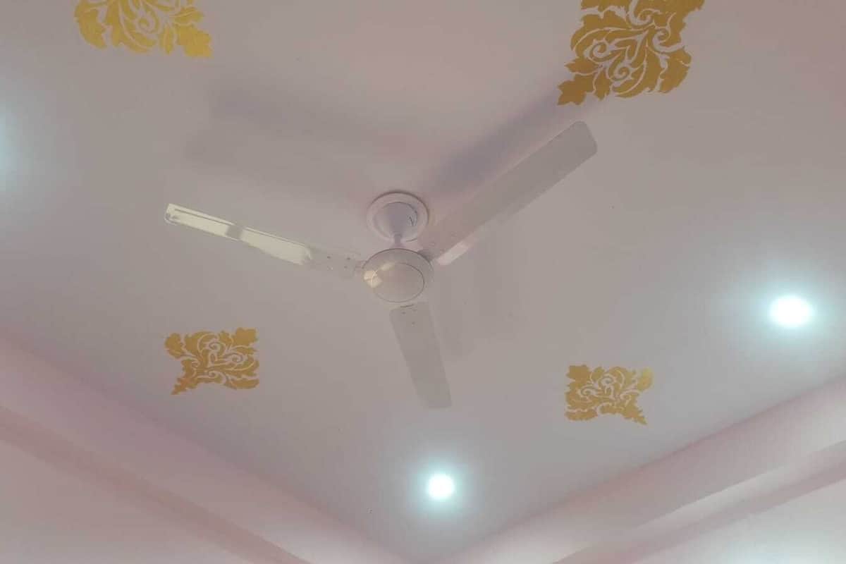 Un ventilador de techo con cuatro luces y diseños dorados decorativos.