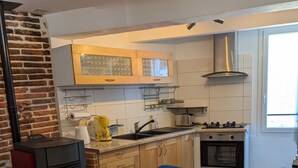 A modern kitchen with a wooden table and chairs, a built-in oven, and a brick wall. - Quiet village house in Alénya - 5km from the beaches (Alénya)