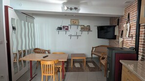 A modern kitchen with a dining area, a TV mounted on the wall, and a brick wall accent. - Quiet village house in Alénya - 5km from the beaches (Alénya)