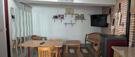 Une cuisine moderne avec un coin repas, un téléviseur fixé au mur et un mur en briques servant d’élément décoratif.
