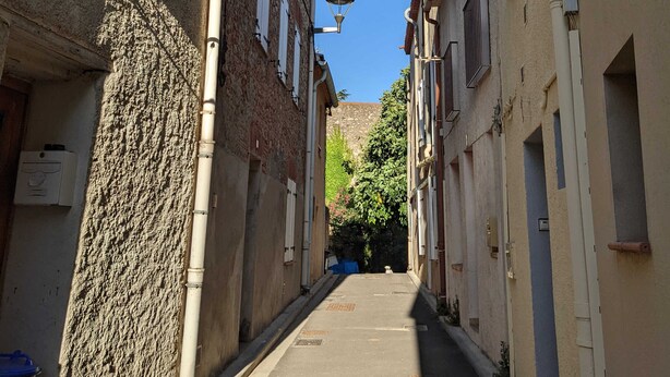 A narrow street with buildings on either side, featuring a mix of brick and plaster facades, and a clear blue sky above. - Quiet village house in Alénya - 5km from the beaches (Alénya)