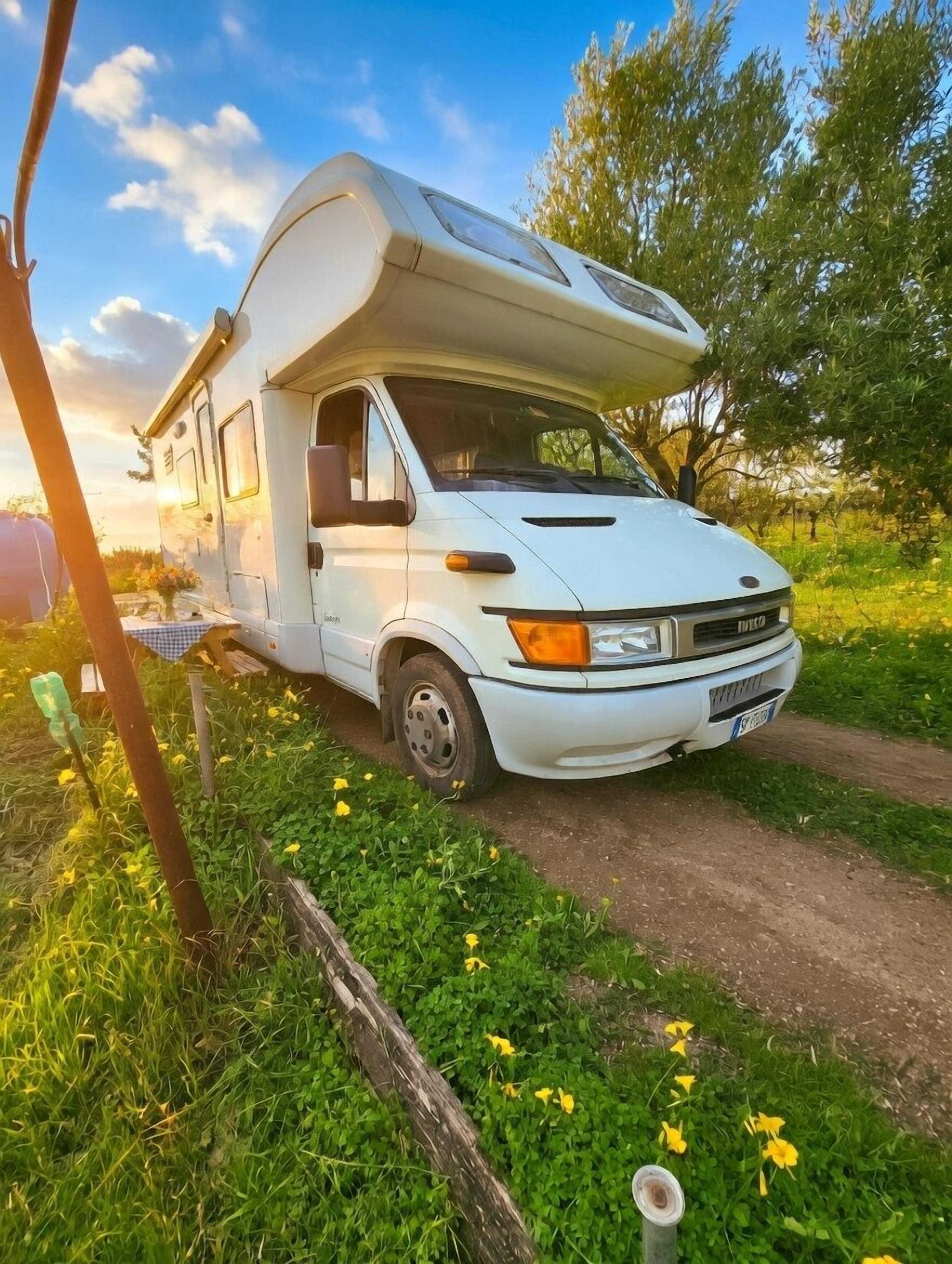 A white camper van parked on a dirt path surrounded by greenery and flowers.