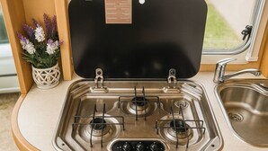 Une cuisine de taille réduite, équipée d’une cuisinière à gaz, d’un évier et d’une fenêtre.