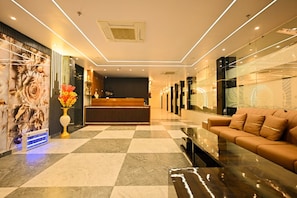 Vestíbulo de hotel con mostrador de recepción, área de registro, un sofá y un muro decorativo con motivos florales.