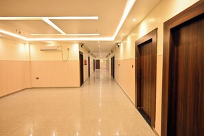 Un corridoio d'hotel con pavimento lucido, porte in legno e illuminazione a incasso.