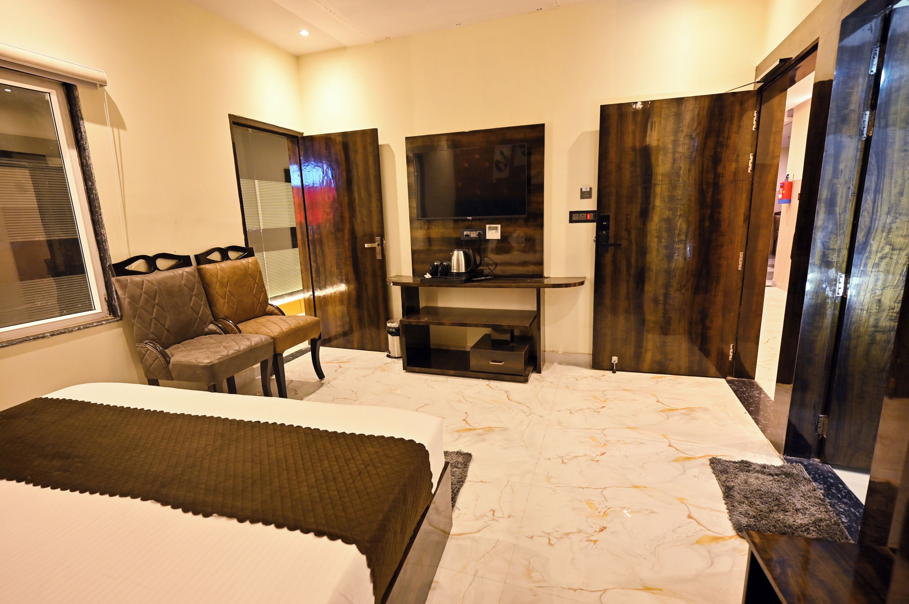 A hotel room with two beds, a television, a desk with a chair, and a window with blinds.