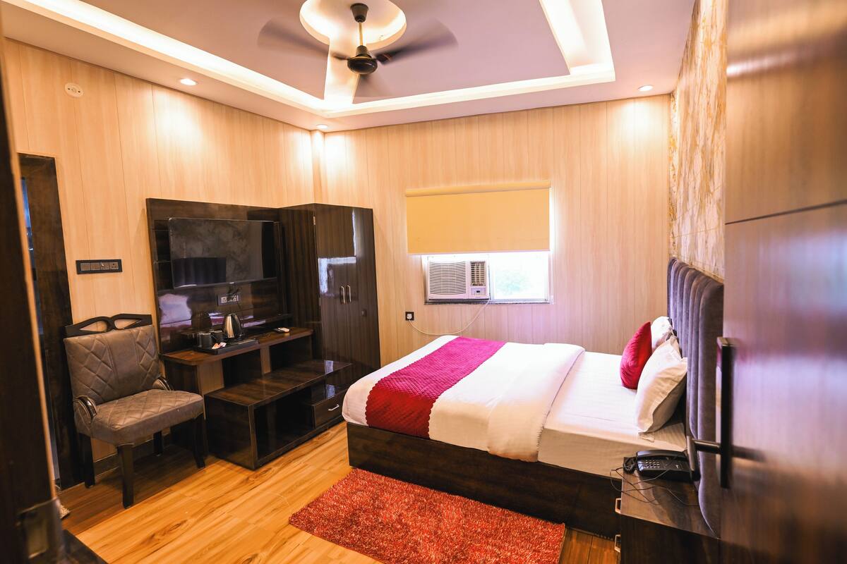 Een hotelkamer met een bed, een bureau, een stoel, een televisie en een plafondventilator.