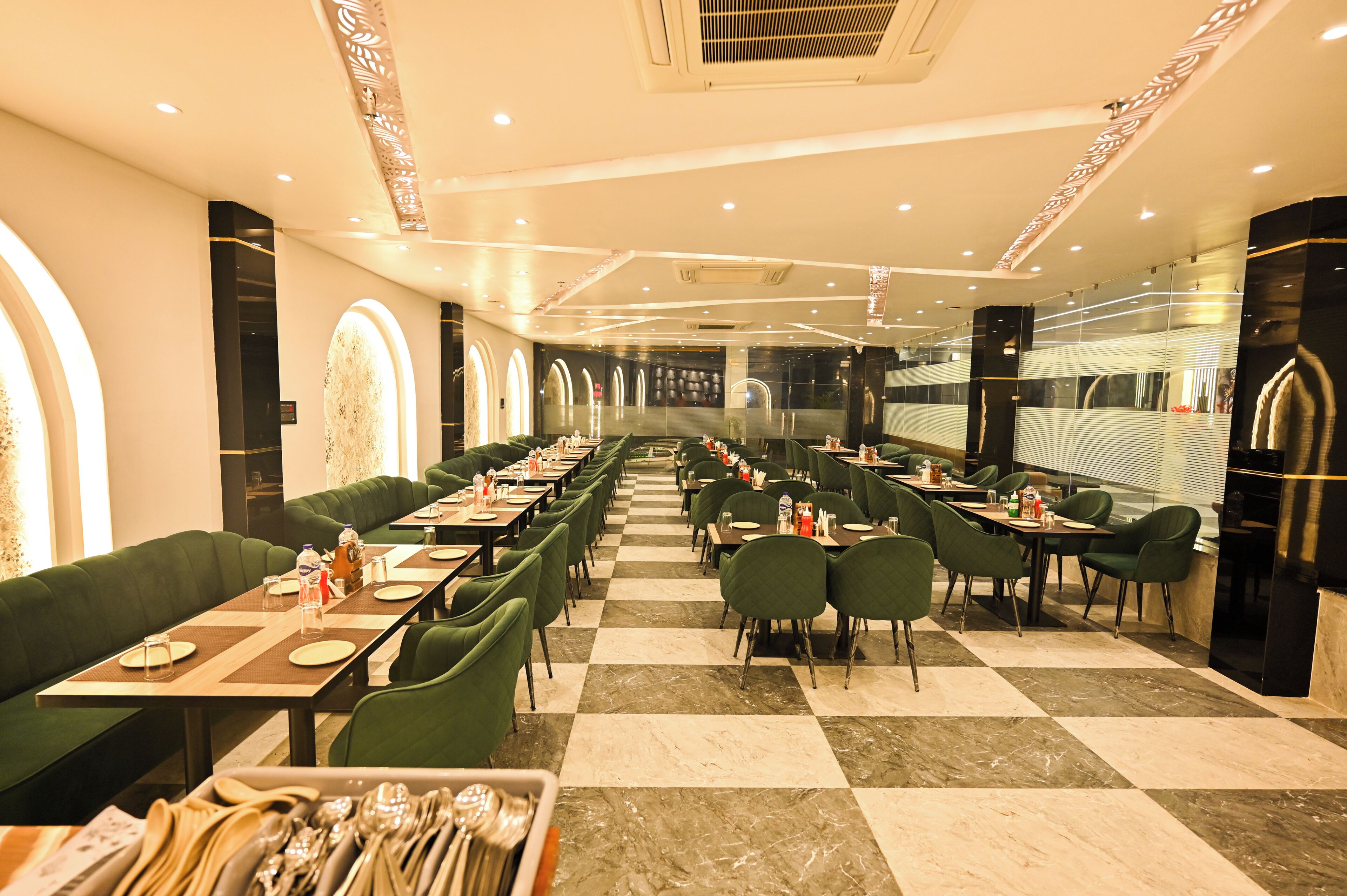 A restaurant with checkered flooring, green upholstered booths, and tables set with cutlery.