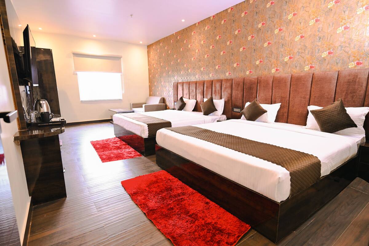 Een hotelkamer met twee bedden, een rood vloerkleed, een televisie en een raam.