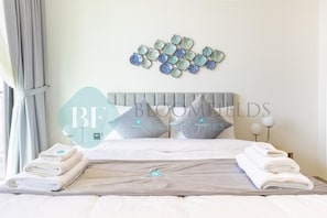 A neatly made bed with folded towels, a headboard, and a wall decoration. - Bloomfields 2BR - Binghatti Onyx - JVC (Dubai)