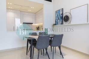A modern kitchen with white cabinets, a dining area with a table and chairs, and artwork on the wall. - Bloomfields 2BR - Binghatti Onyx - JVC (Dubai)