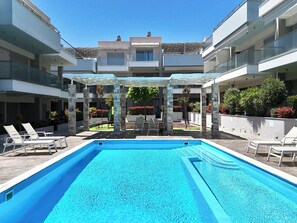 A swimming pool with lounge chairs, a pergola, and a multi-story building in the background.