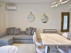 A modern living room with a grey sectional sofa, a dining table with chairs, and two wall-mounted mirrors.