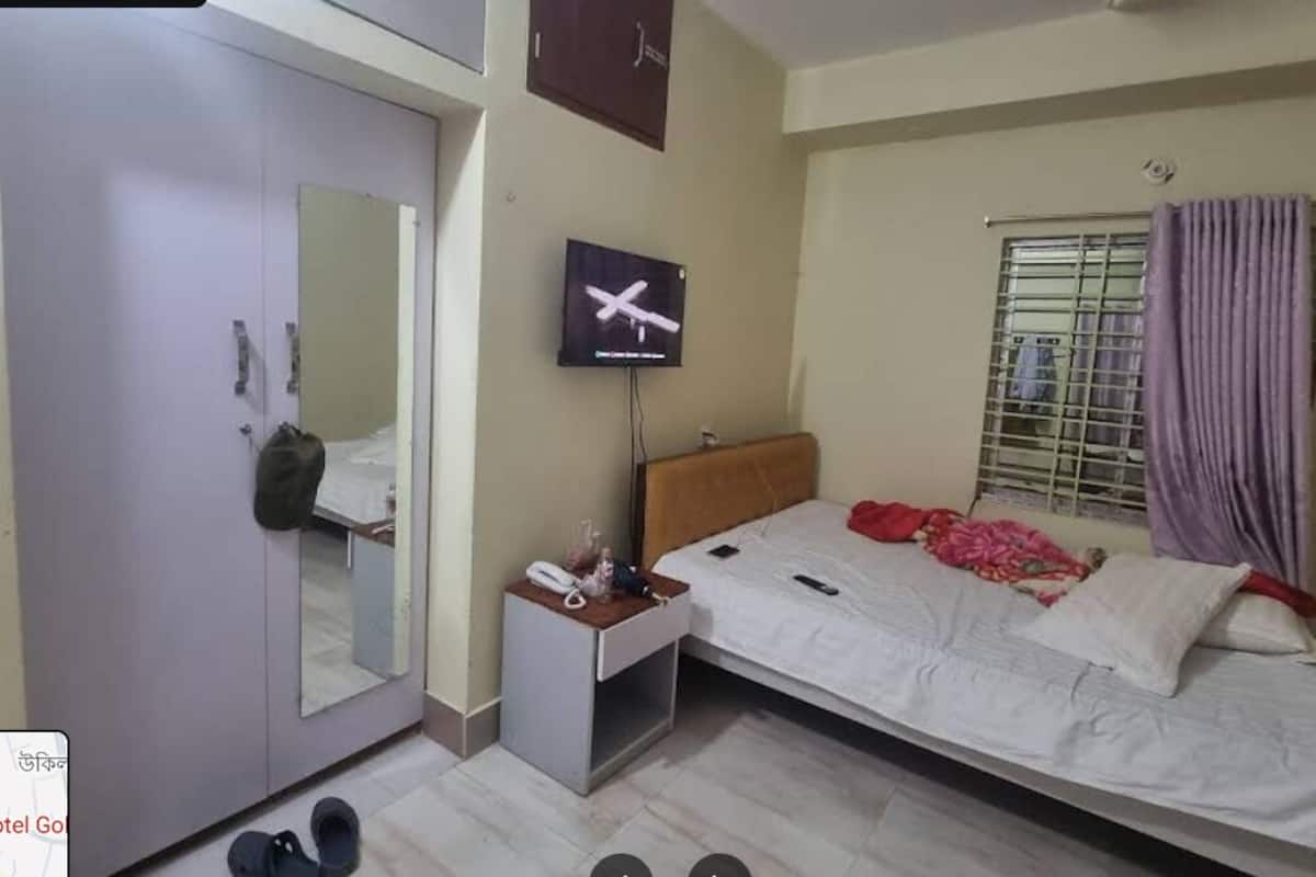 Ein Schlafzimmer mit Bett, Fernseher, Kleiderschrank, Spiegel und einem Fenster mit Vorhängen.
