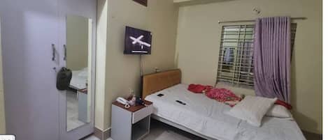 A bedroom with a bed, a TV, a wardrobe, a mirror, and a window with curtains.
