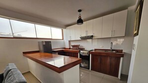 A modern kitchen with a central island, white cabinets, a built-in stove, and a window overlooking a construction site.