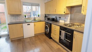 A modern kitchen with wooden cabinets, a dishwasher, a washing machine, a stove, and a window with a view of the outside. - Charming 5-Bedroom Townhouse in Central Gloucester (Gloucester)