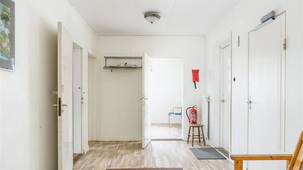 A hallway with white walls, wooden flooring, and a fire extinguisher on a stool. - Family-Friendly Apartment Retreat in Dalarna Sweden (Orsa)