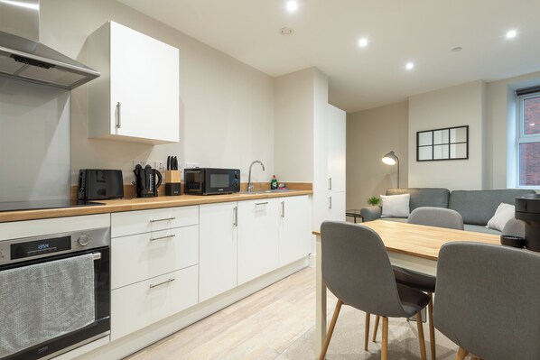 A modern kitchen with white cabinets, a wooden countertop, and a dining area with a table and chairs.